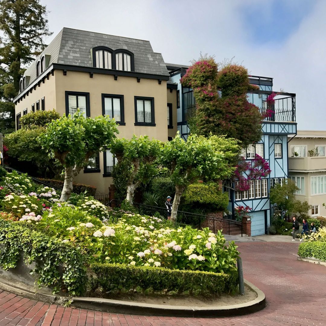Iconic Lombard Street in San Francisco, known for its unique zigzag design. Vibrant hydrangeas and Victorian houses line the winding road under a clear blue sky.